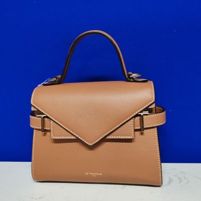 a tan leather handbag with a metal handle on a white table