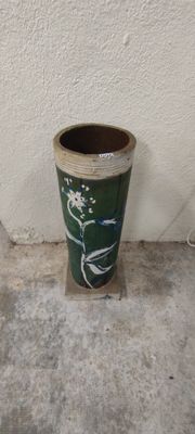 a green vase sitting on a cement floor next to a white wall