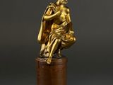 a gold statue of a woman sitting on top of a wooden pedestal