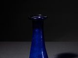 blue glass vase sitting on a table in a dark room