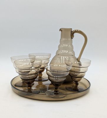 un pichet et six verres posés sur un plateau, avec un autre plateau en dessous