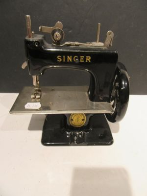 une machine à coudre noire et dorée posée sur une table blanche