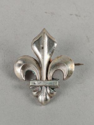 a close up of a metal fleur de lis brooch on a white surface