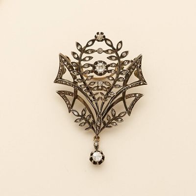 an antique silver broochle with a crystal stone hanging from it ' s center