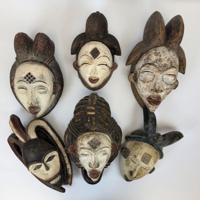 cinq masques africains sont disposés en cercle sur une surface blanche