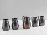 quatre vases noirs sont alignés sur une surface blanche