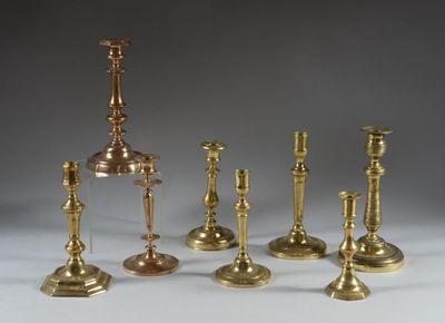 several brass candlesticks are lined up on a white surface
