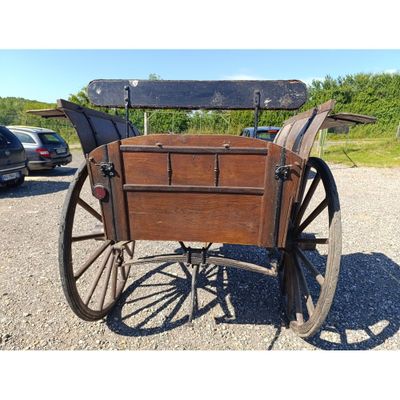 une calèche tirée par un cheval, avec un siège en bois, sur une route en gravier