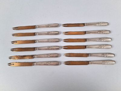 six couteaux argentés sont alignés sur une surface blanche