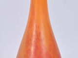 un vase orange et noir posé sur une surface blanche