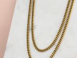 un collier à chaîne en or posé sur une dalle de marbre, sur fond rose