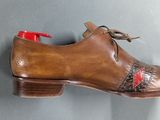 brown leather shoes with red laces hang on a gray wall