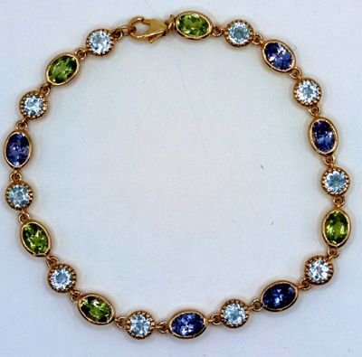 a close up of a gold bracelet with blue and green stones