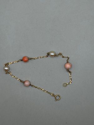 un gros plan sur un bracelet à chaîne en or orné de perles roses et blanches