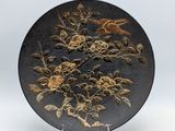 une assiette noire ornée de fleurs et d'oiseaux dorés