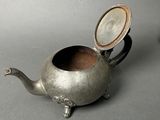 a small silver teapot with a lid on a table