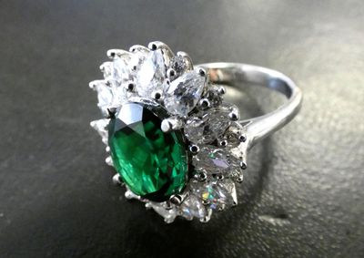 une image d'une bague avec une pierre verte entourée de diamants blancs