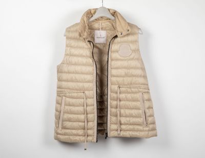 une photo d'un gilet en duvet beige suspendu à un cintre