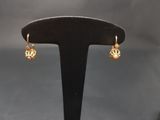 une paire de boucles d'oreilles plaquées or posées sur un présentoir noir