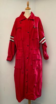 un imperméable rouge posé sur un mannequin, devant un mur blanc