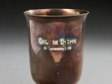 an old silver cup sitting on top of a table next to a black background