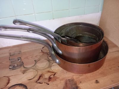 des casseroles et des poêles posées sur un plan de travail en bois dans une cuisine