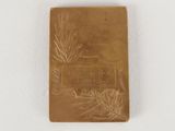 a small gold book with a pine branch on it