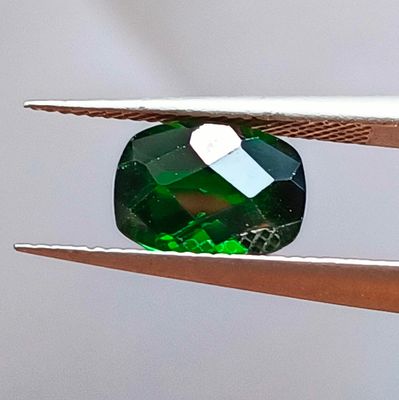 un gros plan d'une pierre précieuse verte tenue par une paire de pinces