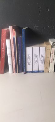 Plusieurs livres sont alignés sur une étagère devant un mur noir