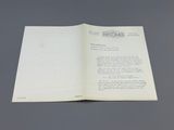 un livre ouvert posé sur une table, sur laquelle se trouve une feuille de papier