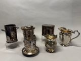 trois tasses en métal argenté et un pichet en métal argenté sur fond blanc