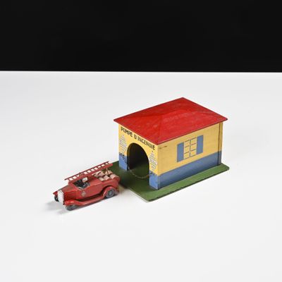 un camion de pompiers miniature et une petite maison posés sur une surface blanche