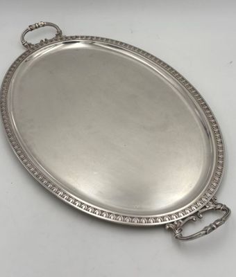 an oval silver tray with handles and beading around the edge