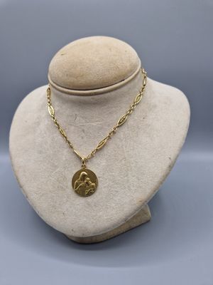 a gold necklace on a mannequin with a coin on it
