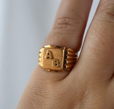 une personne tenant une bague en or sur laquelle est gravée une lettre