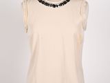 a woman ' s cream top with black beads on the neck