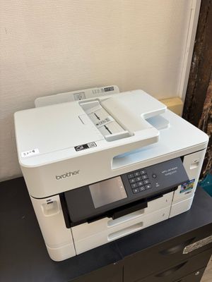 une imprimante blanche posée sur un bureau noir, près d'un mur