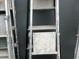 Plusieurs échelles sont alignées contre un mur gris devant un immeuble