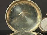 a silver pocket watch sitting on a table next to a clock