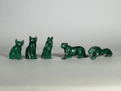quatre figurines de chats verts assises les unes à côté des autres sur une surface blanche