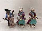 three figurines of monkeys playing musical instruments on a white surface