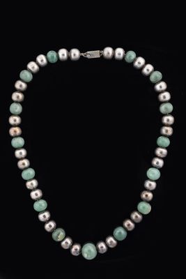 a necklace made of white pearls and green jade beads on a black background