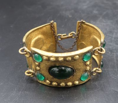 a close up of a gold bracelet with green stones on it