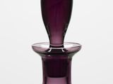 a purple glass bottle with a black top on a table