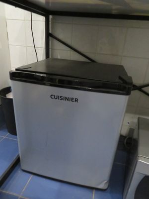 a small white refrigerator sitting on a blue tiled floor
