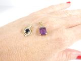 a woman ' s hand with a ring and a ring with a purple stone on it