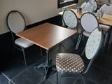 Dans un restaurant au sol carrelé de noir, des tables et des chaises sont alignées.