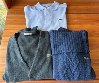 three sweaters are laid out on a wooden table in front of a shelf