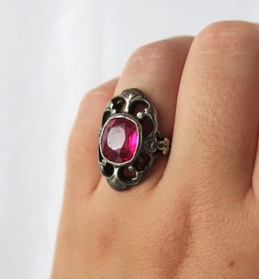 un gros plan sur la main d'une personne tenant une bague sertie d'une pierre rose