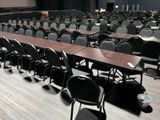 rows of chairs and tables in a large room with a projector screen in the background